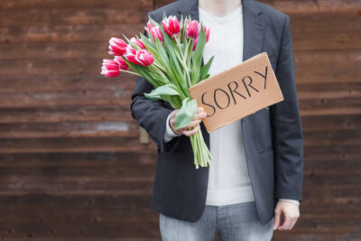 Kann eine Entschuldigung als Schadensersatz reichen? Hier symbolisiert durch einen Mann, der einen Blumenstrauß aus Tulpen sowie ein Schild mit der Aufschrift Sorry in der Hand hält.