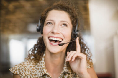 Junge Frau mit Locken spricht lachend in ihr Headset